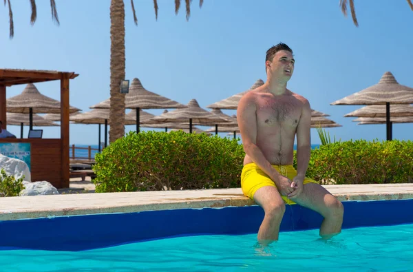 Joven guapo sentado en el borde de la piscina — Foto de Stock