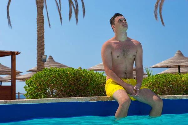 Jeune homme rêvant tout en étant assis sur le bord de la piscine — Photo