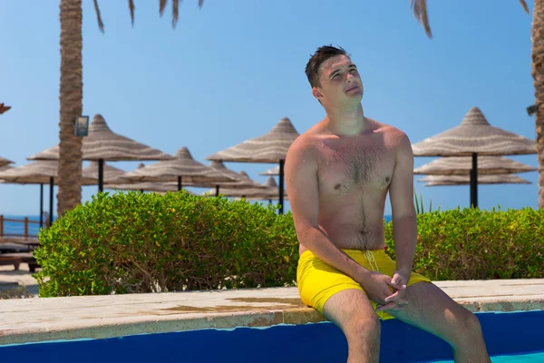 Joven guapo soñando sentado en el borde de la piscina — Foto de Stock