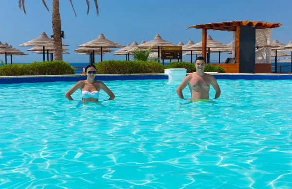 Sonriente pareja joven haciendo aqua fitness en la piscina — Foto de Stock