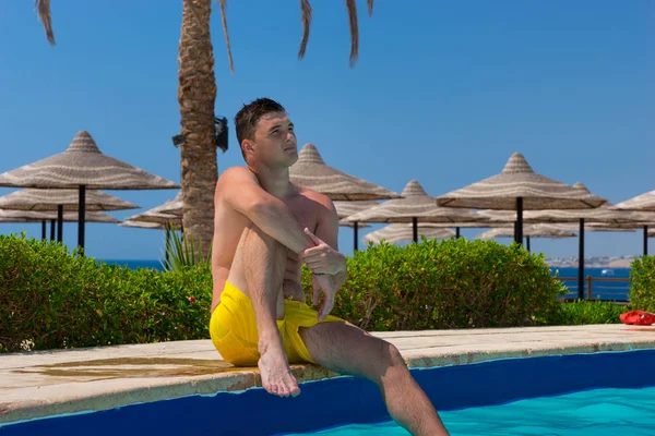 Hombre pensativo guapo sentado en el borde de la piscina — Foto de Stock