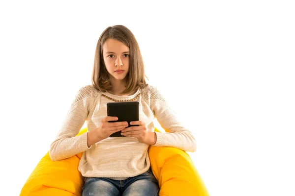 Junges hübsches Mädchen hält die Tablette, während es auf einer gelben Bea sitzt — Stockfoto