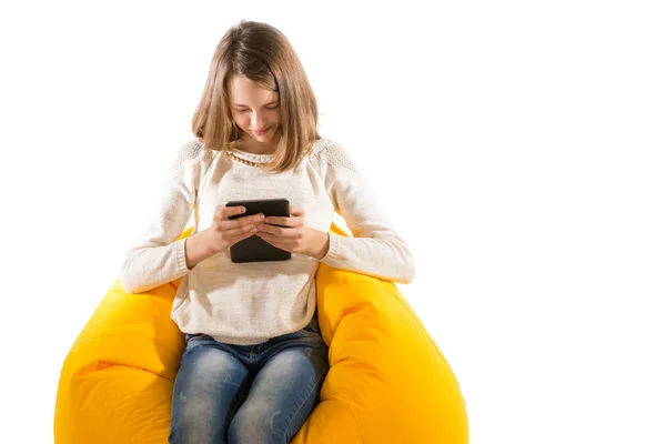 年轻漂亮的女孩坐在黄光上玩这款平板电脑 — 图库照片