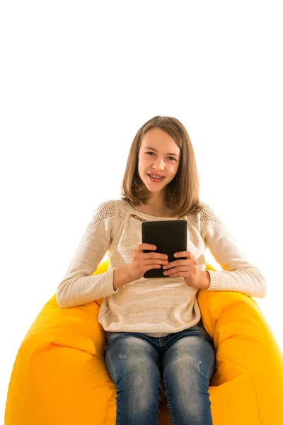 Young smiling girl holding the tablet while sitting on yellow be — Stock Photo, Image