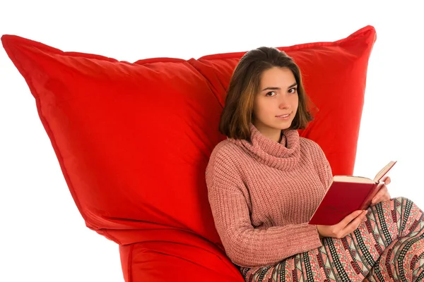 Девушка сидит и читает книгу о красных мешках в форме квадрата — стоковое фото