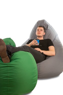 Genç dalgın beanbag sandalye üzerinde yalan ve kahve tutan adam