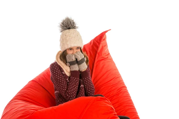 Mädchen in warmem Pullover, Mütze, Schal und Handschuhen auf roter Bohne sitzend — Stockfoto