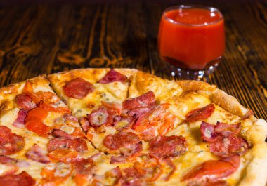 Pepperoni pizza yakınındaki bir bardak domates suyu ile yakın çekim