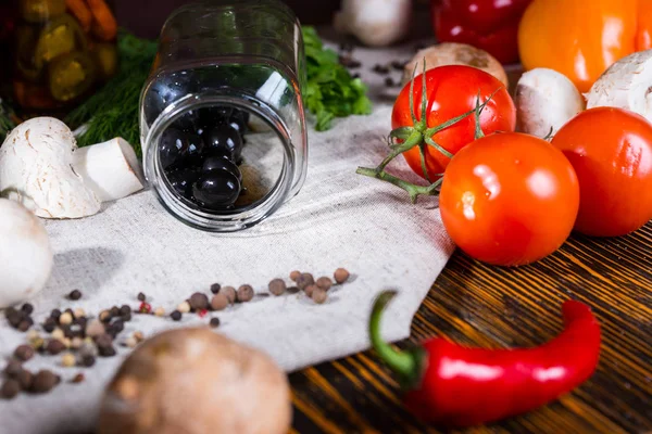 Pot aux olives noires se trouve sur une serviette près des épices et d'autres légumes — Photo