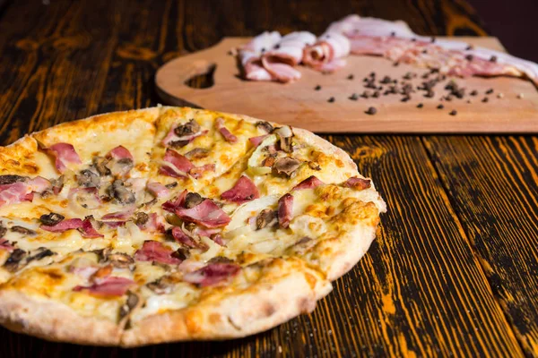 Zbliżenie na pysznej pizzy na drewnianym stole w pobliżu kłamstwo deska do krojenia — Zdjęcie stockowe