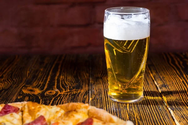 A fából készült asztal, egy pohár sör mellett ízletes pizza — Stock Fotó