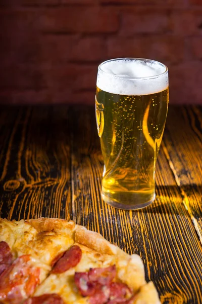 Піца на дерев'яному столі біля келиха пива — стокове фото