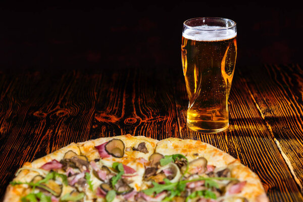 Pizza with ham on wooden table near a glass of beer