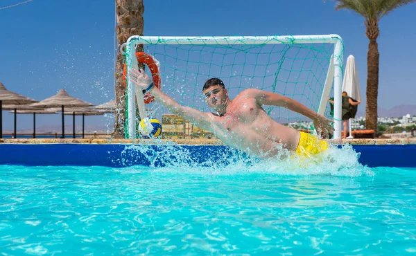 Joven en acción se salta el gol en la piscina jugando waterpolo — Foto de Stock