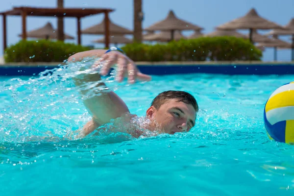 Ung man simma nära bollen i en pool — Stockfoto