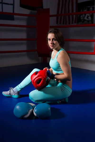 Mujer joven y deportiva sentada cerca de guantes de boxeo y casco — Foto de Stock