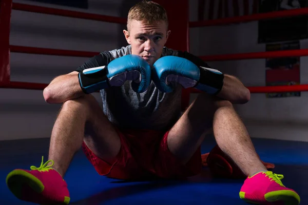 Joven boxeador masculino en guantes de boxeo sentado en el ring de boxeo regular — Foto de Stock