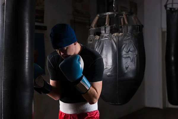 Giovane pugile maschio in cappello e guanti da boxe formazione con boxe — Foto Stock