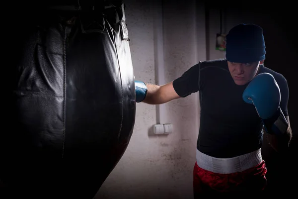 Boxer with stern look in a hat and boxing gloves training with b — Stock Photo, Image