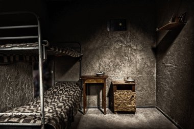Dark empty jail cell with iron bunk bed and wooden bedside table clipart