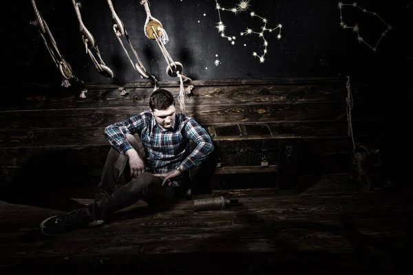 Disappointed man sits near a chest, holding glass bottle and try — Stock Photo, Image
