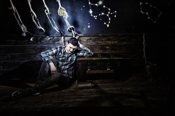 Disappointed guy sits near a chest, holding glass bottle and try — Stock Photo, Image