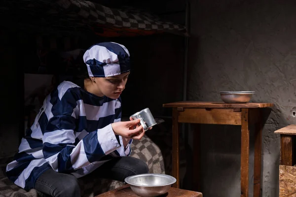 Prisonnière en uniforme de prisonnière assise sur un lit et contre — Photo