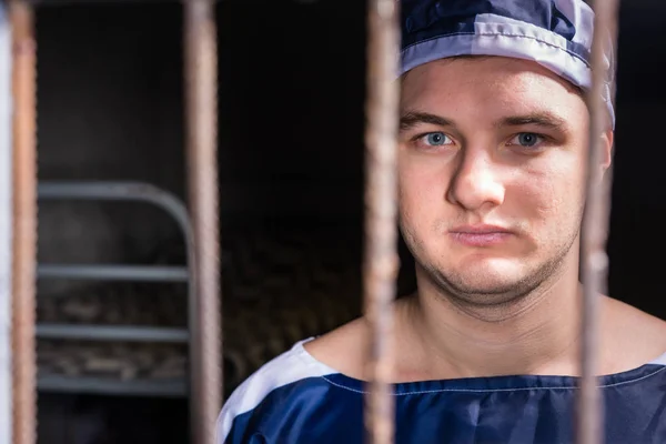 Portrait of young male prisoner standing behind a prison grid in — Stock Photo, Image