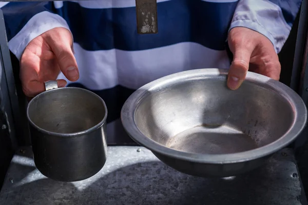 Prisoner's hands holding aluminum dishes in a hole for supplying — Stock Photo, Image