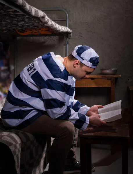 Prisioneiro usando uniforme de prisão lendo um livro ou uma bíblia enquanto — Fotografia de Stock