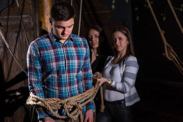 Junge Frauen binden einen jungen traurigen Kerl an eine Säule auf dem Deck eines Shi — Stockfoto