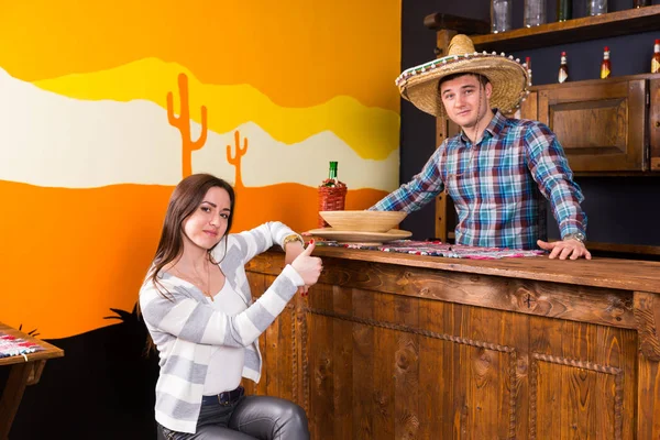 Young woman with thumbs up sitting at the bar counter next to th — Stock Photo, Image