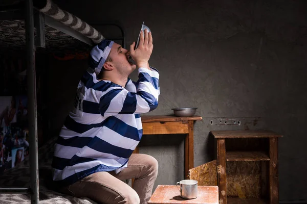Мужчина заключенный сидит на кровати и ест из алюминиевой тарелки в — стоковое фото