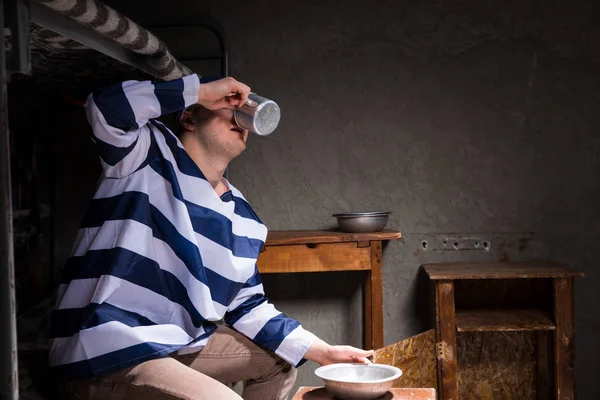 Чоловік в'язень п'є з алюмінієвої чашки в невеликій в'язниці — стокове фото