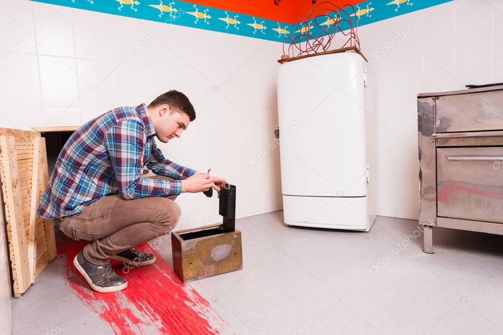Young guy in plaid shirt squatting and opening the safe trying t