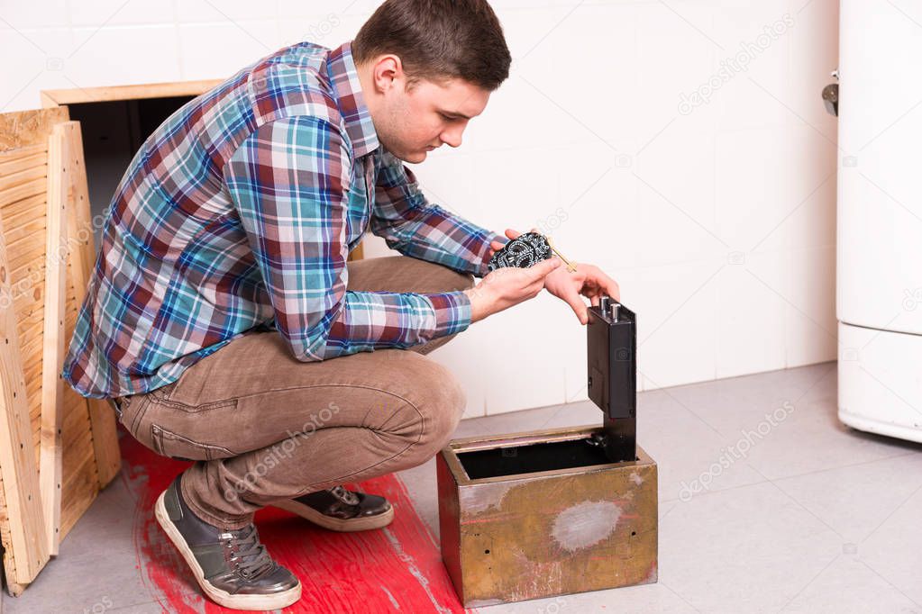 Young guy squatting and opened the safe looks at the puzzle tryi