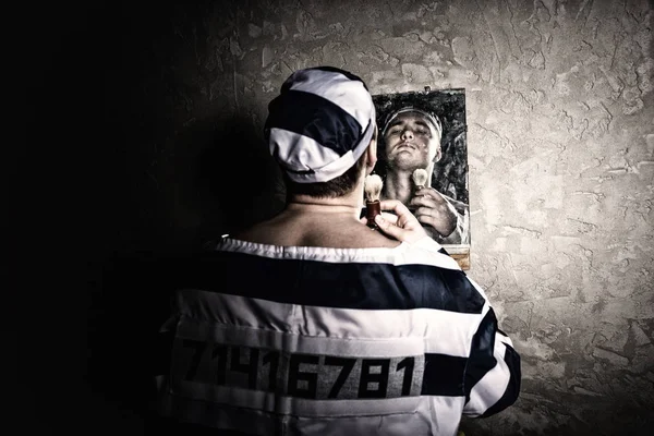 Чоловік ув'язнений стоїть з щіткою для гоління і дивиться на його відображення — стокове фото