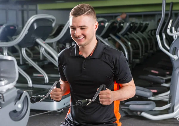 Handsome smiling fit man training on modern row machine in gym — Stock Photo, Image