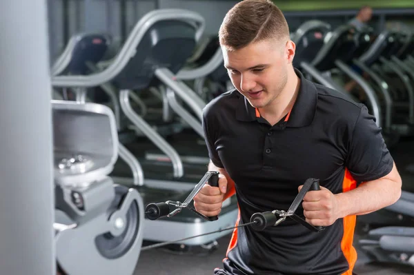 Bonito homem em forma de treinamento na moderna máquina de fileira no ginásio — Fotografia de Stock