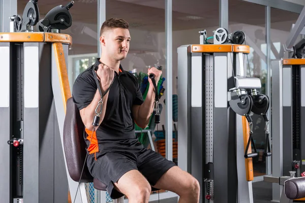 Hombre guapo entrenando en la máquina moderna y haciendo ejercicio en el gimnasio — Foto de Stock