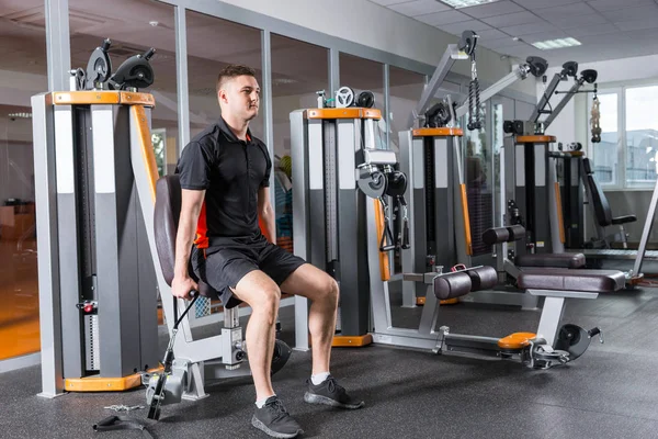 Handsome fit man training on modern machine and working out in g — Stock Photo, Image