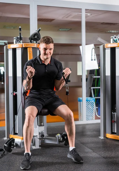 Jovem homem apto a treinar na máquina moderna e exercitar-se no ginásio — Fotografia de Stock