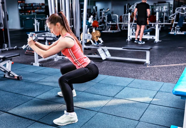 Young sportive woman in sportswear doing squat and holding dumbb — Stock Photo, Image