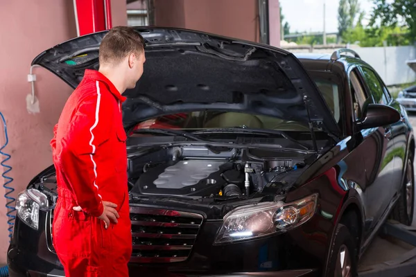 Young male motor mechanic in uniform standing near a black sedan — Stock Photo, Image