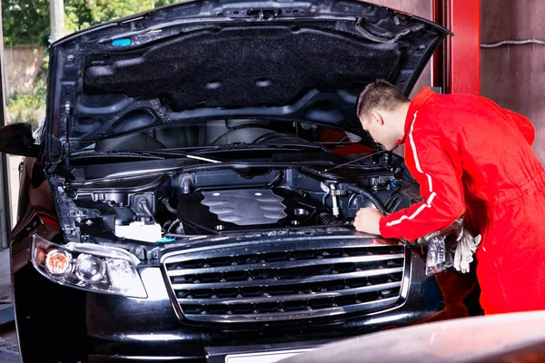 Young male motor mechanic in uniform checking and fixing car eng — Stock Photo, Image
