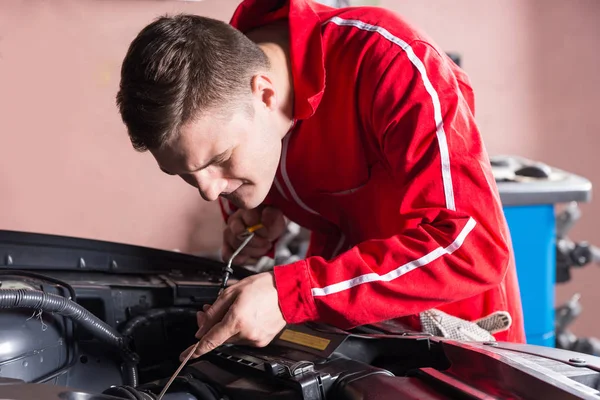 Jovem mecânico verificando o nível de óleo em um motor de carro — Fotografia de Stock