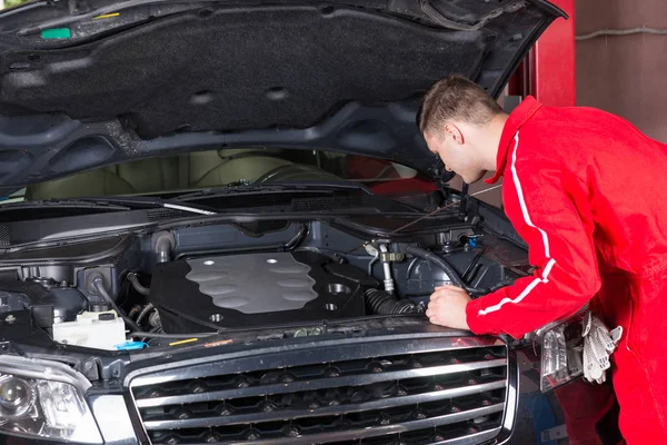 Автомеханик в форме, проверка и ремонт автомобильного двигателя — стоковое фото