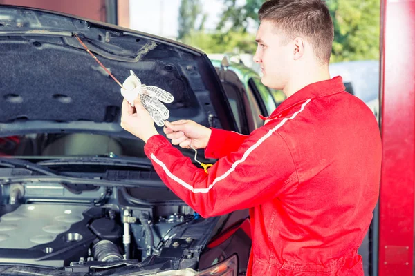 Young handsome mechanic wipes with a glove the dipstick after ch — Stock Photo, Image