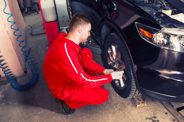 Concentrated male auto mechanic sitting near a black sedan and s — Stock Photo, Image