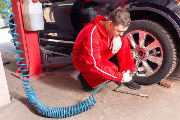 Young male auto mechanic checking the air pressure of a tyre — Stock Photo, Image